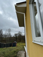 Белый водосток Döcke Premium ПВХ крупным планом на жёлтой стене