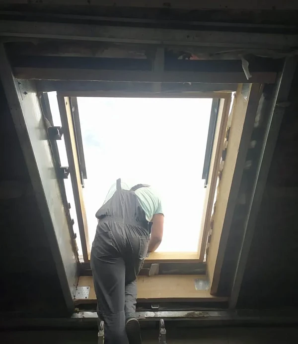 Монтажник устанавливает мансардное окно в металлический каркас