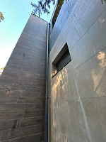 Угол здания с облицовкой из керамогранита и водосточной трубой